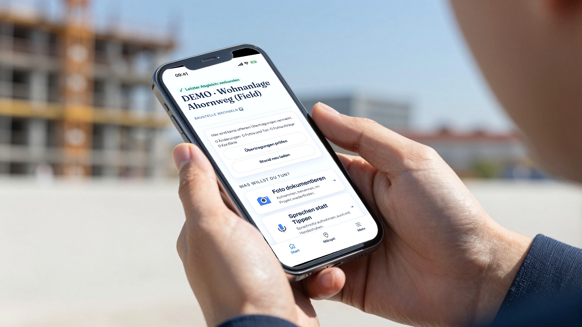 Hände halten auf einer Baustelle ein Smartphone, auf dem die Startseite der Gewerkton-App mit Vorführprojekt zu sehen ist